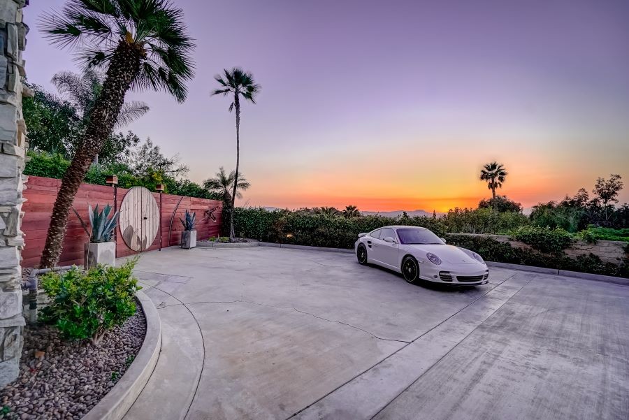 A car in a driveway outside a gated-house at sunset.