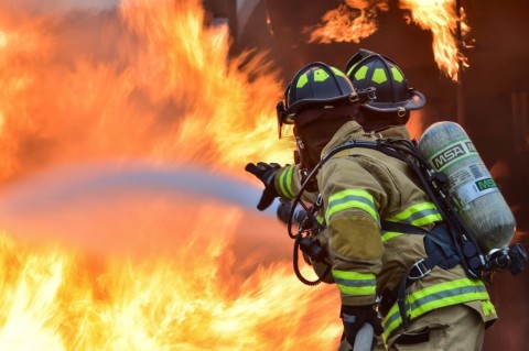 Two firefighters streaming water from a firehose towards a large fire.