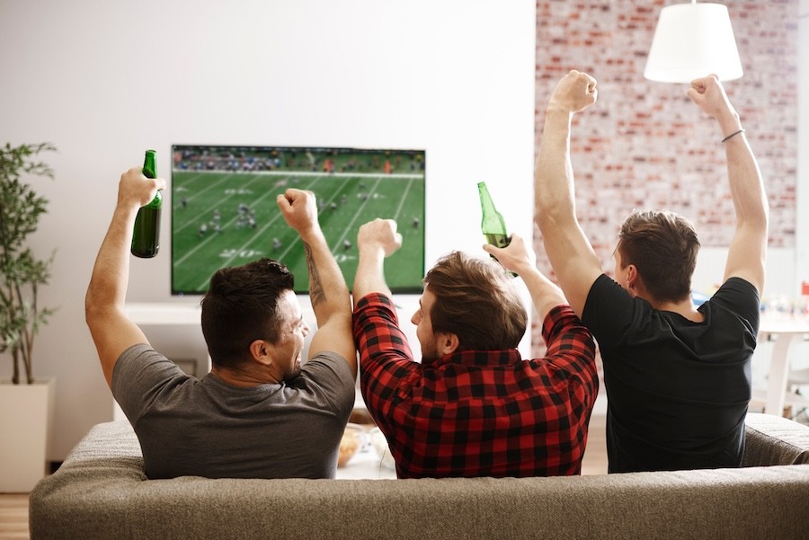 Guys cheering on the couch, watching a football game on TV.