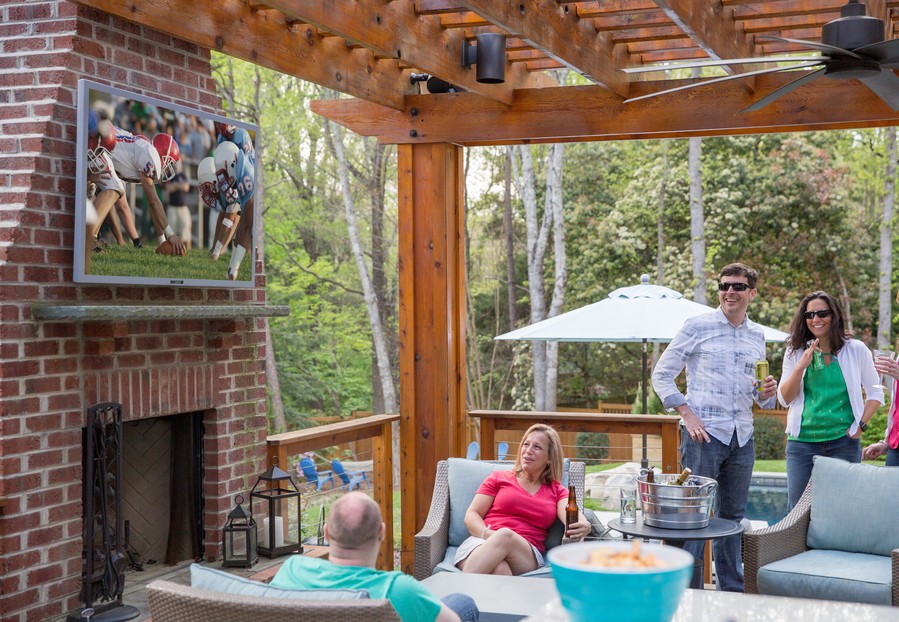 A group of people on the patio watching football on an outdoor SunBrite TV.